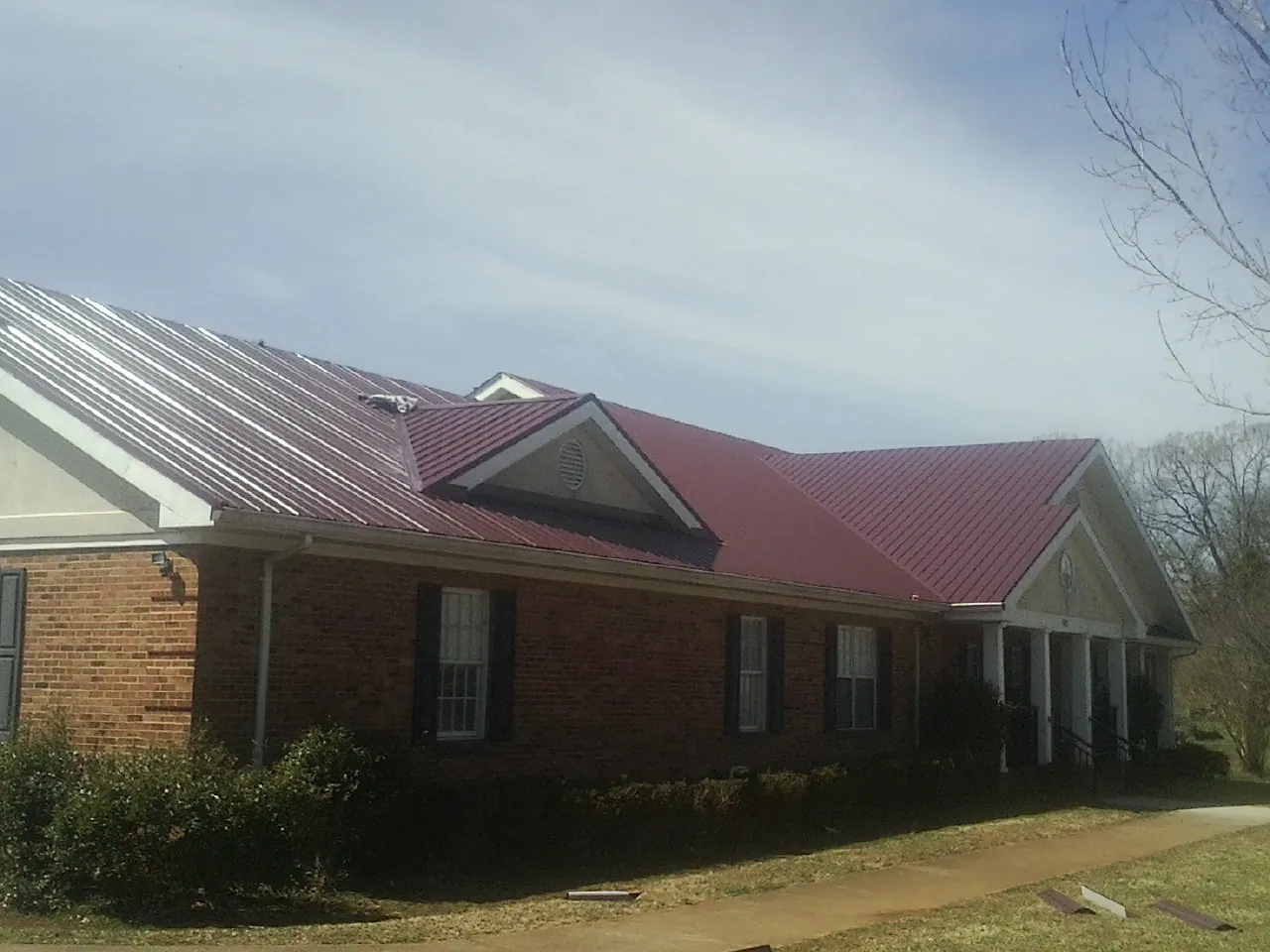 Red metal roof with gabled entries on a long brick building, from a Hail Damage Roof Repair job in Elk Grove Village