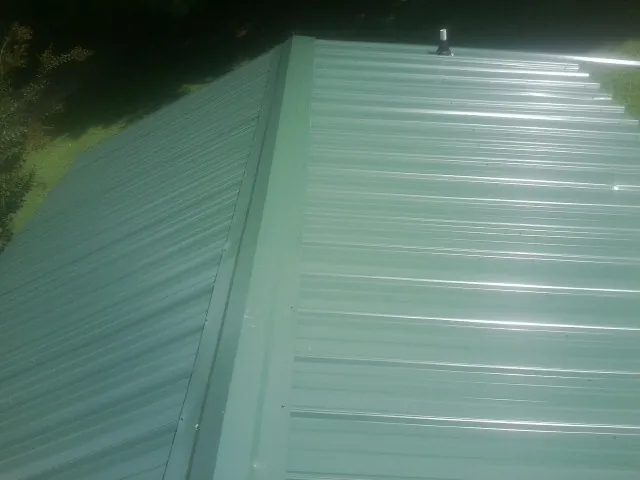 New green metal panels meeting at the ridge of a roof — Flat Roof Repair work by our crew in Elk Grove Village