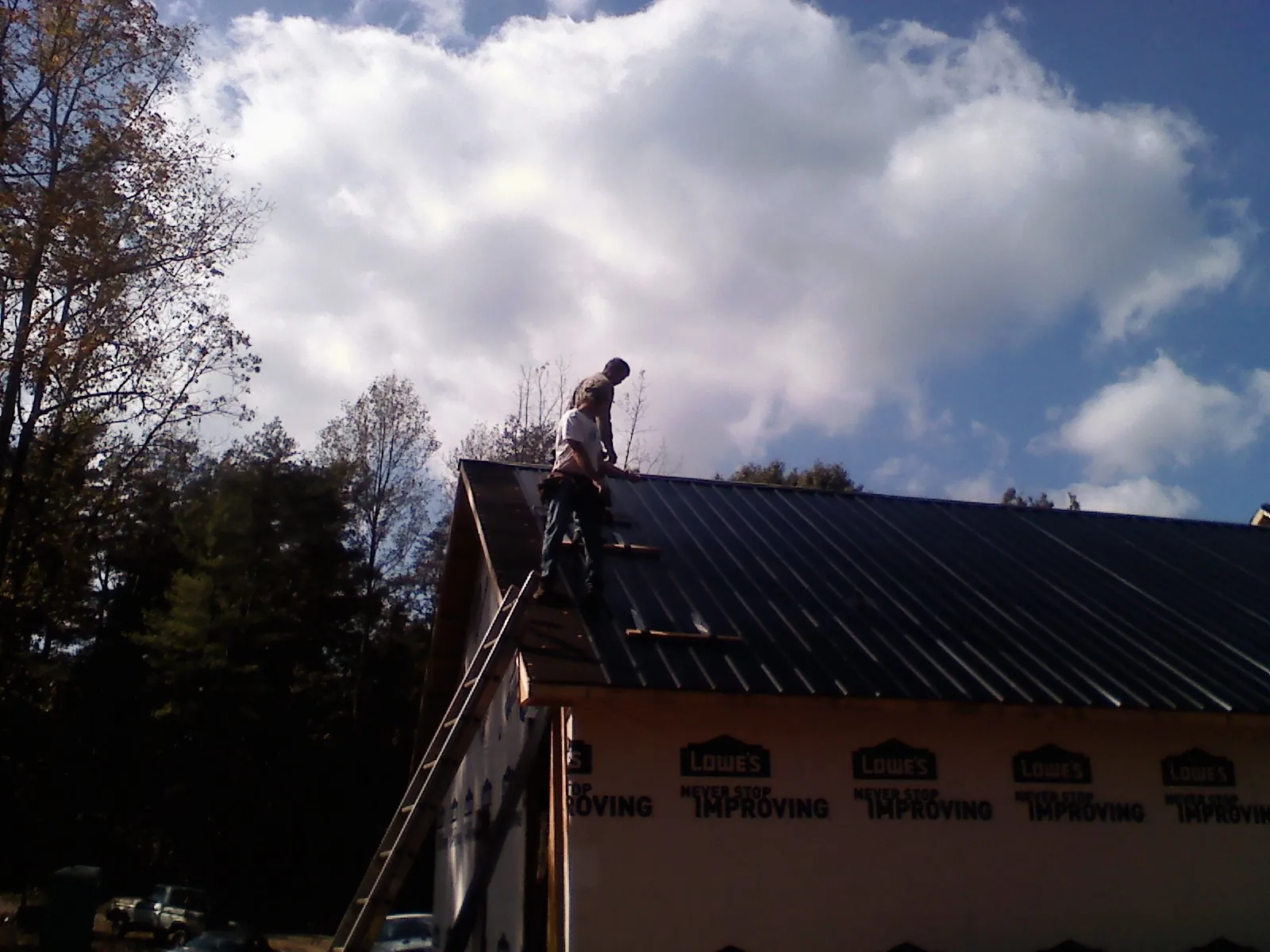 Roofer fastening dark metal panels high against a cloudy sky, from a Roof Inspection job in Elk Grove Village